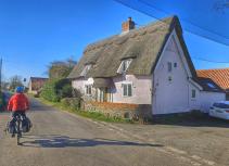 Cycling past a thatched cottage Norfolk